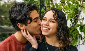 Un hombre de alto valor besa tiernamente a su pareja, rodeados de vegetación.