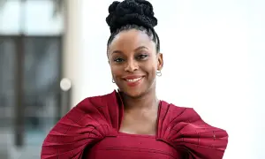 Chimamanda Ngozi Adichie, una de las escritoras famosas más influyentes, sonríe con un peinado recogido y un vestido rojo.