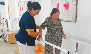 Terapeuta ayuda a anciana a caminar con barras paralelas, un paso importante en varias áreas de la vida.