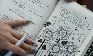 Un diario abierto muestra dibujos de girasoles y la frase "PLANT A GARDEN FULL OF SELF LOVE, GIRL!". Es un ejemplo de que es journaling, una práctica para la autoexpresión.