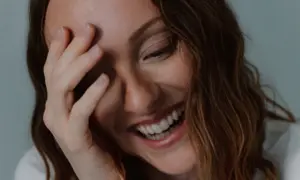 Una mujer ríe a carcajadas, cubriendo su rostro con la mano, un momento de pura labilidad emocional.