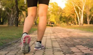 Piernas de una persona caminando por un sendero de adoquines en un parque, con el objetivo de caminar 10 km diarios.