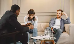 Terapia de pareja: un hombre habla con una mujer angustiada, mientras su pareja escucha con la mano en la cabeza.