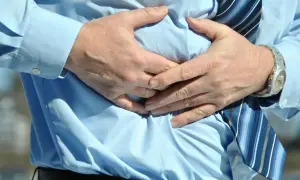 Hombre con camisa azul y corbata a rayas, sujetándose el abdomen por una **sensación de vacío en el estómago**.