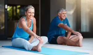 Pareja sonriente haciendo ejercicio en casa, estirando las piernas en una esterilla azul.