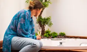 Mujer con copa de champán, disfrutando del slow living junto a una bañera y plantas.