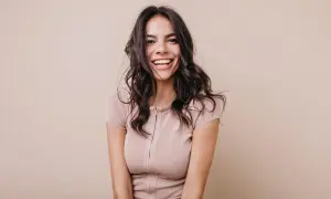 Mujer sonriendo con cabello oscuro y ondulado, luciendo un vestido beige. Su expresión irradia confianza, un ejemplo del "pretty privilege".