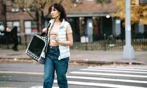 Mujer con bolso y café cruza la calle, lista para aplicar las 7 reglas para adelgazar caminando.
