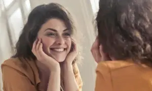 Una mujer sonríe a su reflejo, preguntándose "quien soy" mientras se mira en el espejo.