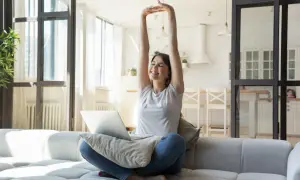 Joven estirándose en el sofá con un portátil, lista para cambiar su rutina y empezar el día con energía.