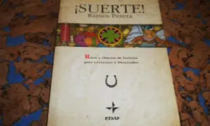 El libro de la buena suerte, "¡Suerte!" de Ramos Perera, explora ritos y objetos de fortuna. Incluye una herradura y un trébol.