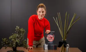 Mujer sonriente con suéter rojo, sosteniendo un libro sobre el cuerpo y la digestión, promoviendo el body positive.