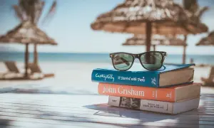 Gafas de sol sobre una pila de libros para leer en inglés, con la playa y el mar de fondo.