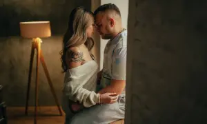 Una pareja se abraza tiernamente, sus frentes juntas. Ella tiene un tatuaje de flor en el hombro. Esto es hacer el amor de verdad: conexión y ternura.