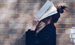 Una persona se esconde detrás de un libro abierto, disfrutando de los beneficios de la lectura.