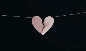 Corazón de papel rosa roto, colgado de un hilo, simbolizando los síntomas del desenamoramiento.