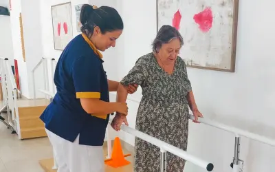 Terapeuta ayuda a anciana a caminar con barras paralelas, un paso importante en varias áreas de la vida.
