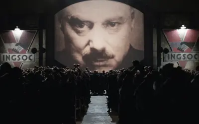 Multitud ante pantalla gigante con el rostro de un hombre y el logo de INGSOC. Un eco de las **1984 frases** que controlan sus mentes.