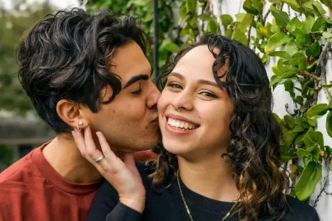 Un hombre de alto valor besa tiernamente a su pareja, rodeados de vegetación.