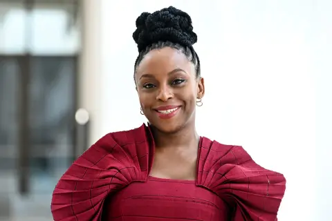 Chimamanda Ngozi Adichie, una de las escritoras famosas más influyentes, sonríe con un peinado recogido y un vestido rojo.