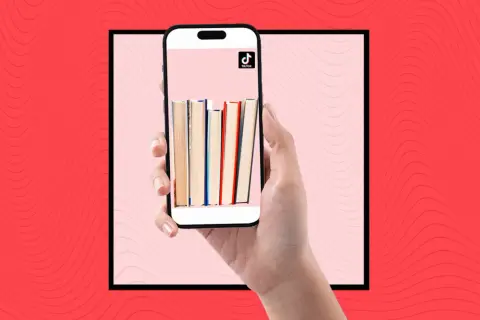 Una mano sostiene un teléfono con libros en la pantalla, mostrando la comunidad de **que es booktok** y sus recomendaciones literarias.