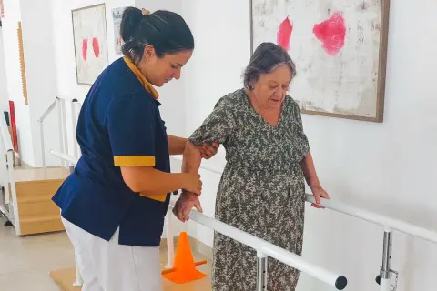 Terapeuta ayuda a anciana a caminar con barras paralelas, un paso importante en varias áreas de la vida.