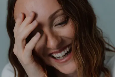 Una mujer ríe a carcajadas, cubriendo su rostro con la mano, un momento de pura labilidad emocional.
