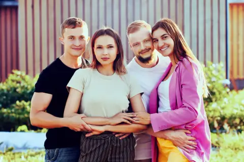 Dos parejas sonríen, unidas en un abrazo que ilustra el poliamor que es, una conexión amorosa y respetuosa entre varias personas.