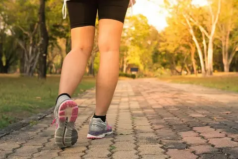 Piernas de una persona caminando por un sendero de adoquines en un parque, con el objetivo de caminar 10 km diarios.