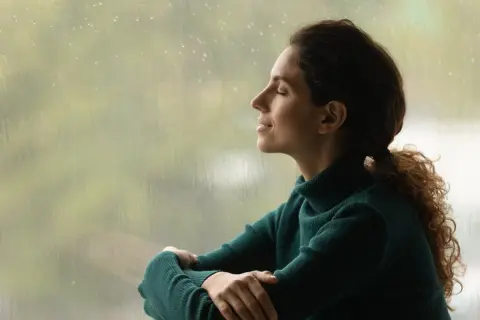 Mujer con los ojos cerrados, disfrutando de la lluvia y la paz interior.