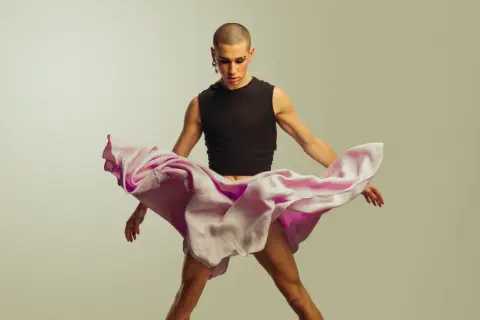 Joven con maquillaje y falda rosa ondeante, desafiando la masculinidad frágil.
