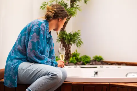 Mujer con copa de champán, disfrutando del slow living junto a una bañera y plantas.