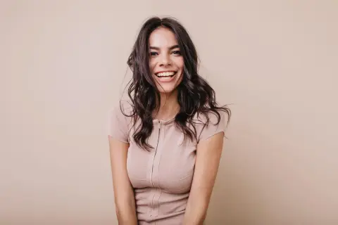 Mujer sonriendo con cabello oscuro y ondulado, luciendo un vestido beige. Su expresión irradia confianza, un ejemplo del "pretty privilege".