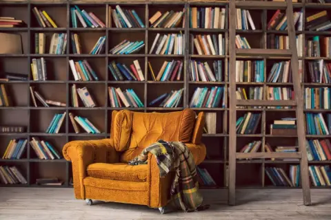 Un sillón acogedor y una manta a cuadros esperan en este rincón perfecto para un club del libro. Estanterías llenas de libros invitan a la lectura.