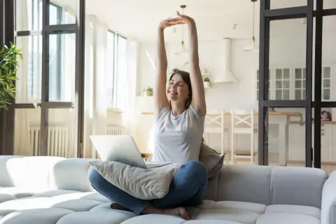 Joven estirándose en el sofá con un portátil, lista para cambiar su rutina y empezar el día con energía.