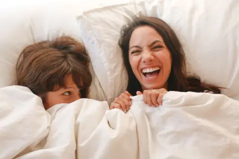 Dos personas riendo bajo las sábanas. Una pregunta que es ser asexual, es una forma de amar sin necesidad de contacto físico.