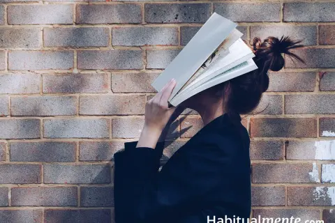 Una persona se esconde detrás de un libro abierto, disfrutando de los beneficios de la lectura.