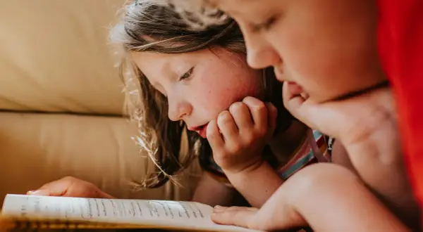 Dos niños concentrados en la lectura de un libro, ideal para lectura para niños de 10 a 12 años.
