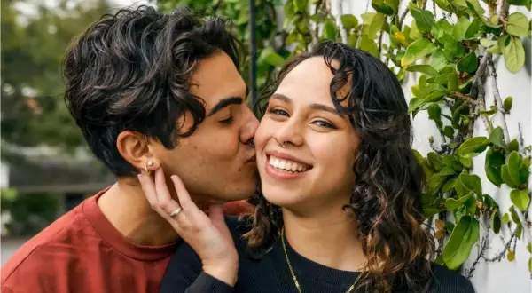 Un hombre de alto valor besa tiernamente a su pareja, rodeados de vegetación.