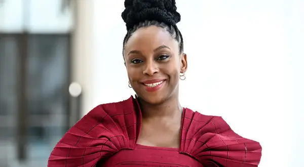 Chimamanda Ngozi Adichie, una de las escritoras famosas más influyentes, sonríe con un peinado recogido y un vestido rojo.