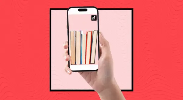 Una mano sostiene un teléfono con libros en la pantalla, mostrando la comunidad de **que es booktok** y sus recomendaciones literarias.