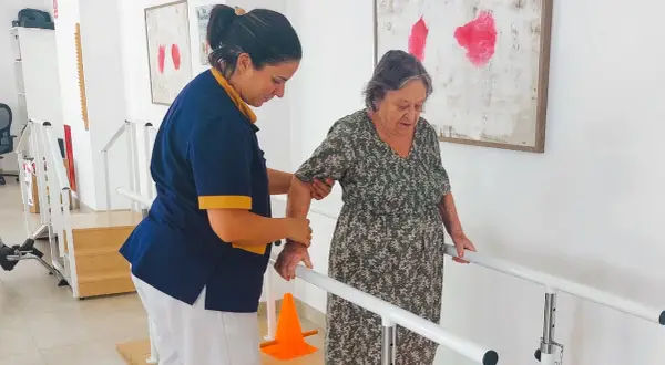 Terapeuta ayuda a anciana a caminar con barras paralelas, un paso importante en varias áreas de la vida.