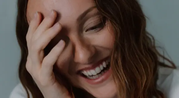 Una mujer ríe a carcajadas, cubriendo su rostro con la mano, un momento de pura labilidad emocional.