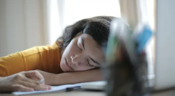 Joven con hipersomnia que es, duerme sobre sus brazos en un escritorio, con un lápiz en la mano.