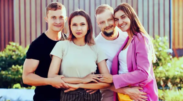 Dos parejas sonríen, unidas en un abrazo que ilustra el poliamor que es, una conexión amorosa y respetuosa entre varias personas.