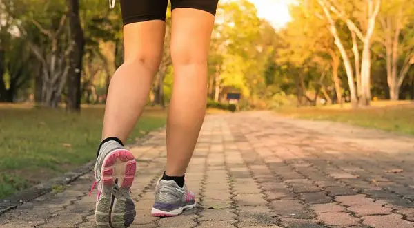 Piernas de una persona caminando por un sendero de adoquines en un parque, con el objetivo de caminar 10 km diarios.