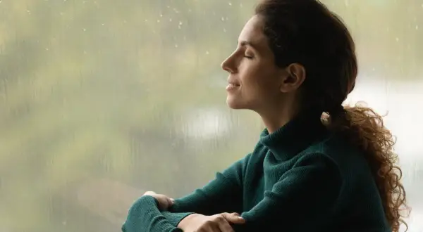 Mujer con los ojos cerrados, disfrutando de la lluvia y la paz interior.