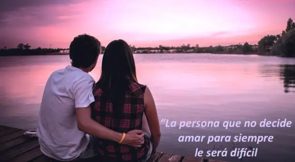 Pareja abraza en muelle al atardecer. La frase "existe el amor para toda la vida" inspira, sugiriendo que la decisión de amar siempre es clave.
