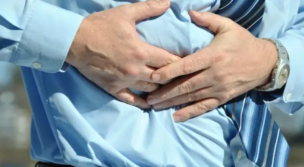 Hombre con camisa azul y corbata a rayas, sujetándose el abdomen por una **sensación de vacío en el estómago**.