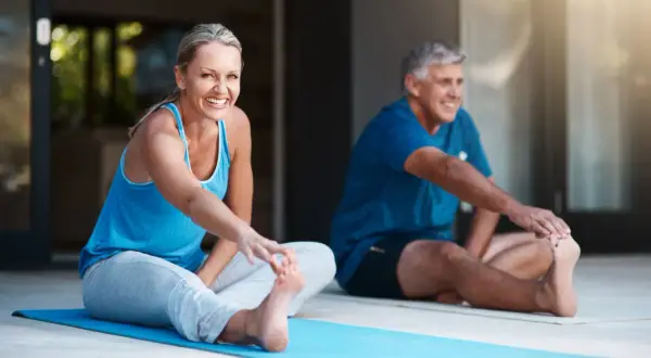 Pareja sonriente haciendo ejercicio en casa, estirando las piernas en una esterilla azul.